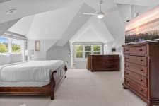 A bedroom featuring a wooden sleigh bed, dark dressers, and vaulted ceilings with large windows.
