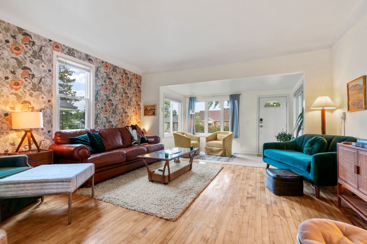 Relax in your stylish living room with rich leather sofa, vibrant teal velvet chair, and beautiful floral wallpaper creating the perfect ambiance.