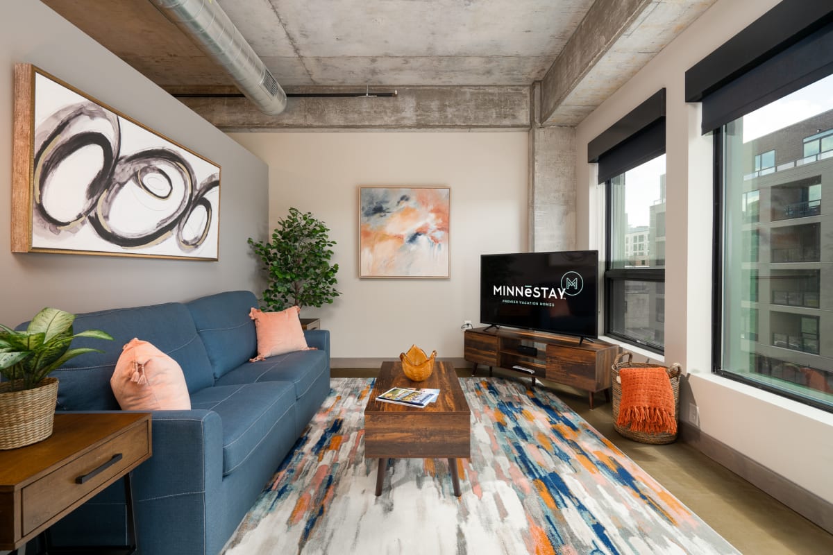 Unwind in your stylish living space with exposed concrete ceilings, vibrant artwork, and floor-to-ceiling windows flooding natural light throughout.