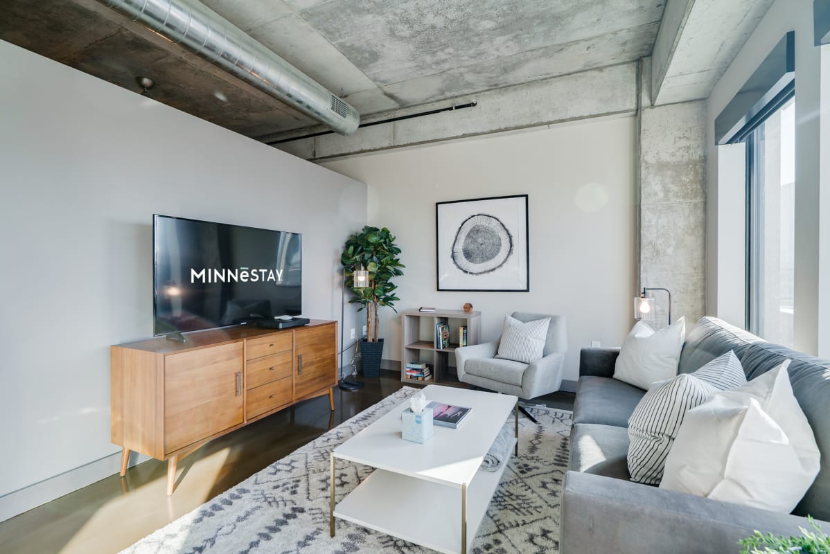 Relax in your industrial-chic living room featuring exposed concrete, modern sectional seating, and stylish decor for ultimate urban comfort.