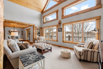 A rustic living room with high wooden ceilings and large windows overlooking nature.