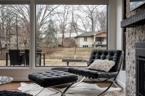 Modern interior space with a black leather chair and a view of trees and a backyard through large windows.
