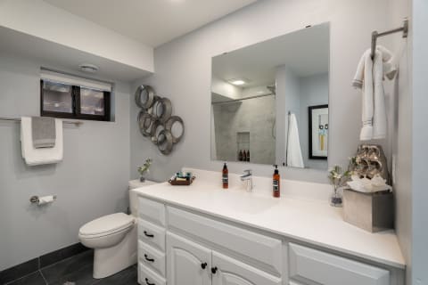 A modern bathroom with white cabinetry, sleek mirror, and dark flooring.