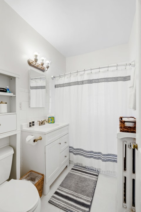 A modern bathroom featuring a white shower curtain, a vanity with a sink, and a cozy striped rug.