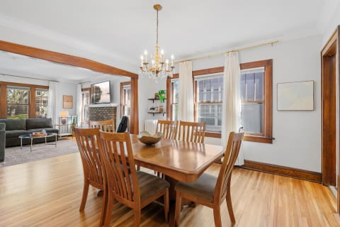 Dining area with wooden table and chairs, chandelier above, and visible living room.