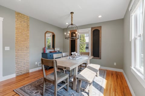 A rustic dining room featuring a wooden table, benches, and a blue sideboard, illuminated by a chandelier.