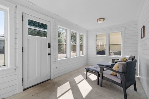 A sunroom with white walls, a white door, dark wicker chairs, and large windows.