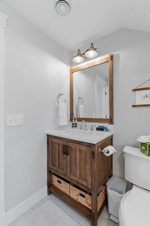 Modern bathroom featuring a wooden vanity with a white countertop and stylish light fixtures.