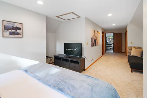 A spacious bedroom featuring a bed with a blue throw, a flat-screen TV, and artwork on the wall.