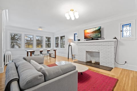 Living room with a gray sofa, white brick fireplace, and dining table.