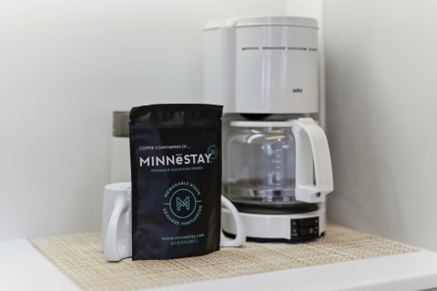A modern coffee maker next to a black coffee bag from MINNESTAY, displayed on a kitchen counter.