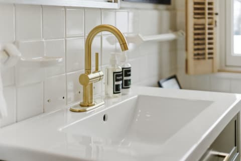 Modern bathroom sink with gold faucet and white tiles.