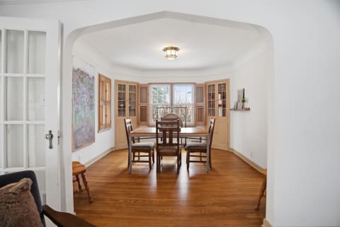 A bright dining room with wooden floors, built-in cabinets, and a central dining table surrounded by chairs.