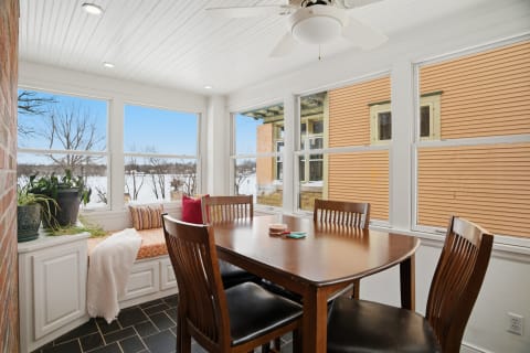 Cozy dining area with a wooden table, chairs, window seat, and winter views.