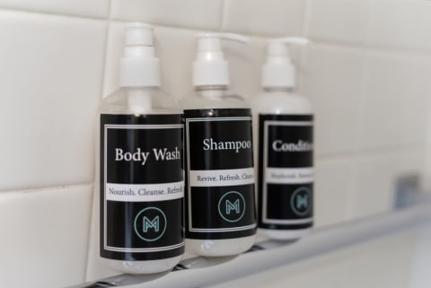 Three bottles of premium toiletries – body wash, shampoo, and conditioner – arranged on a sleek shelf in a modern bathroom.