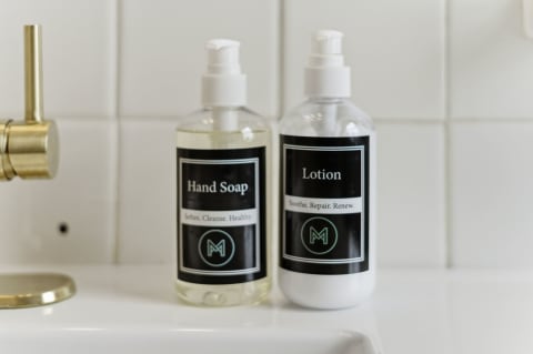 Stylish hand soap and lotion bottles on a bathroom sink with gold faucet.