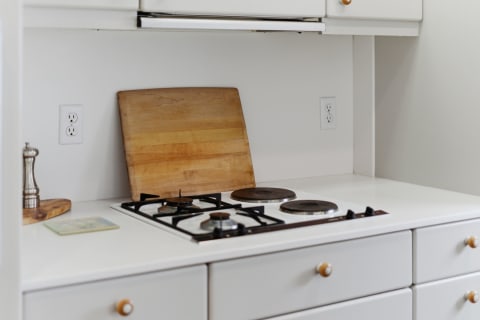Sleek white kitchen with modern gas burners and a wooden cutting board.
