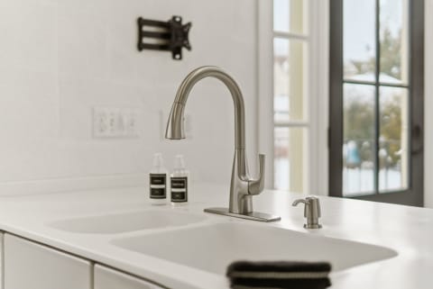 Stylish kitchen sink featuring a stainless steel faucet, soap dispensers, and a sleek white countertop.