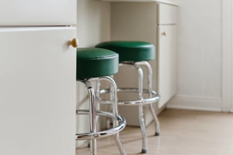 Two green bar stools with chrome legs situated near a kitchen island.