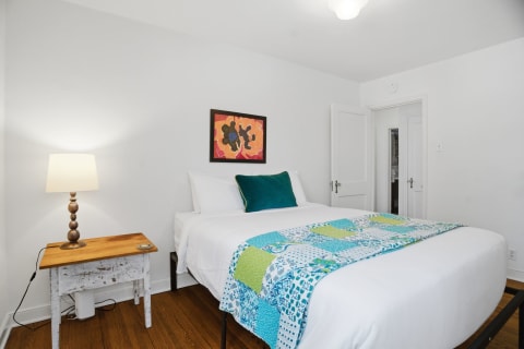 A cozy bedroom featuring white linens, colorful accents, and warm wooden flooring.