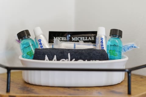 A welcome basket filled with toiletries including shampoo, conditioner, toothpaste, and a washcloth on a wooden surface.