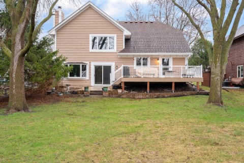 Two-story house with brown siding and a deck overlooking a grassy yard.