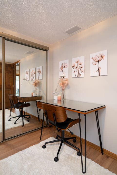 A modern workspace with a glass desk, black chair, and floral wall art.