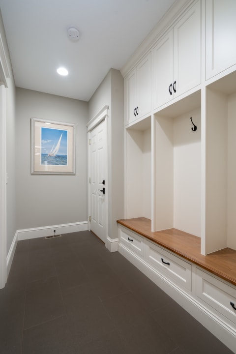 Interior view of a mudroom with white storage units, a wooden bench, and a nautical painting on the wall.