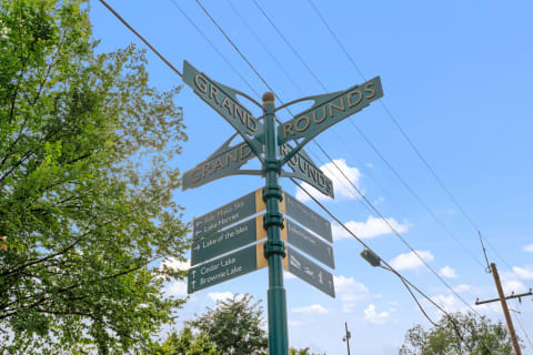 A decorative signpost labeled 'Grand Rounds' with directions to local lakes against a blue sky.