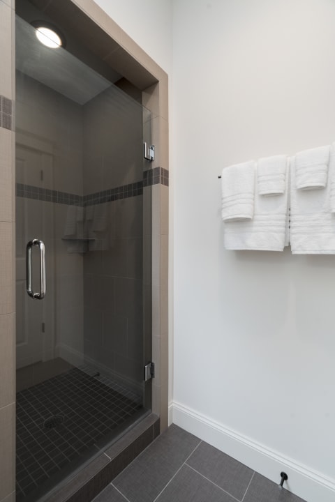 A stylish bathroom with a glass shower, gray tiles, and white towels.