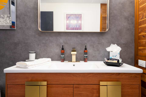 Modern bathroom vanity with wooden cabinet, gold faucet, and decorative items.