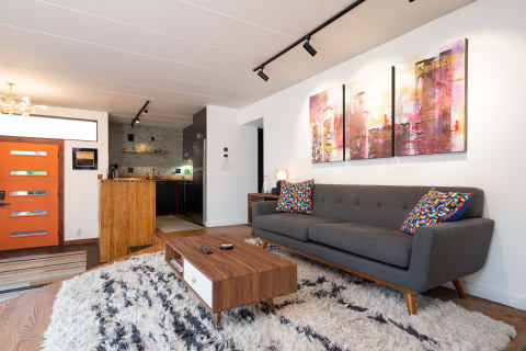 Modern living room with gray sofa, colorful cushions, coffee table, and abstract paintings.