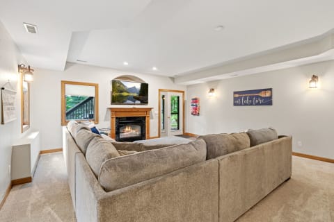 Cozy living room featuring a large gray sofa, fireplace, and flat-screen TV displaying a mountain scene.