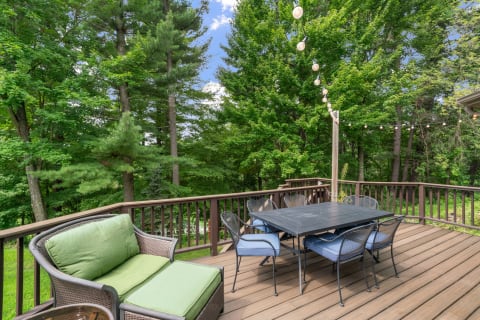 Outdoor deck with a green couch and a black dining table, surrounded by trees.