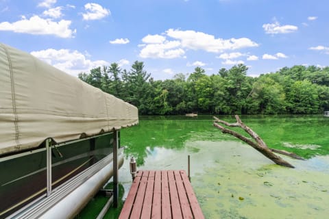 Lakeside view featuring a wooden dock and covered boat under a blue sky.