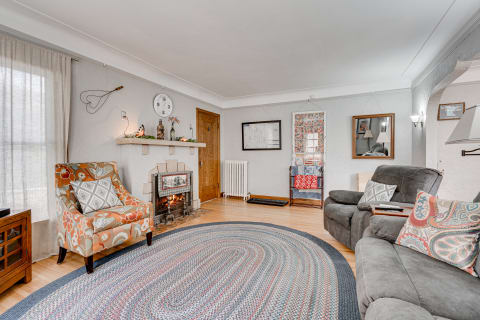 A beautifully designed living room with a cozy feel, featuring a floral armchair, braided rug, and a fireplace.