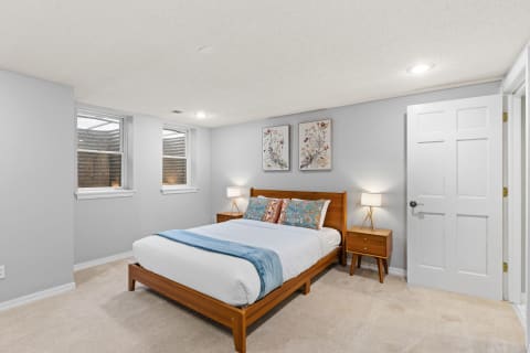 A tranquil bedroom featuring a wooden bed, side tables with lamps, and floral artwork.