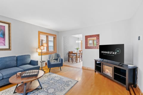 A modern living room with a blue sofa, wooden coffee table, and a TV displaying MINNESTAY branding.