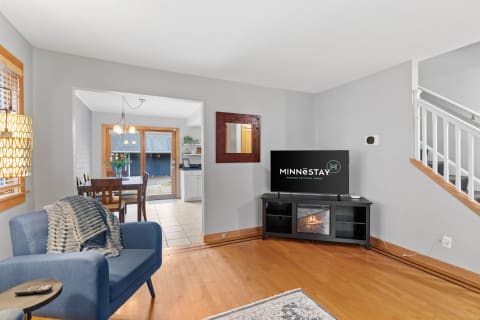 Inviting living room with a blue armchair, TV unit, and adjacent dining area, showcasing warm wooden floors and soft lighting.