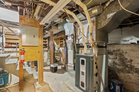 A mechanical room in a basement featuring a furnace, electrical panel, and utility infrastructure.