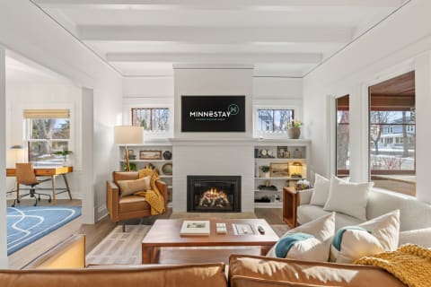 A bright and cozy living room with a fireplace, comfortable seating, and a workspace, designed for relaxation.