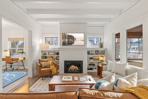 Modern living room with a fireplace, cozy seating, and a workspace filled with natural light.