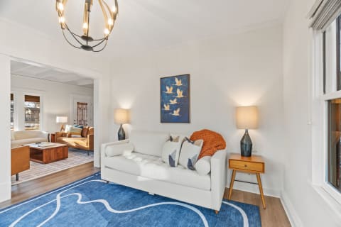 A stylish living room featuring a white sofa, blue rug, and artwork of birds, illuminated by warm lighting.