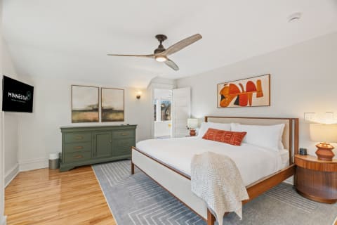 View of a stylish, serene bedroom featuring a king-sized bed, decorative artwork, and a green dresser.