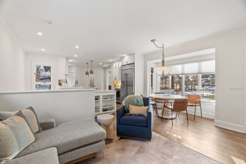 Inviting open-plan living space featuring a cozy sectional sofa, modern kitchen appliances, and a round dining table by large windows.