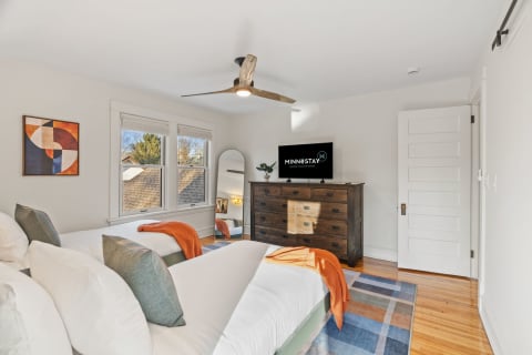 Stylish twin bedroom with orange accents, a TV, and natural light from windows.