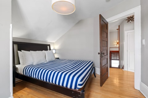 A cozy attic bedroom featuring a striped mattress, wooden flooring, and an open door leading to another space.