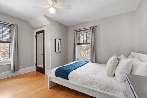 A bright and inviting bedroom with a white bed, blue blanket, and wooden floors.