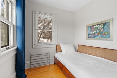 A serene bedroom with a wooden bed, white bedding, and a vibrant floral painting on the wall.