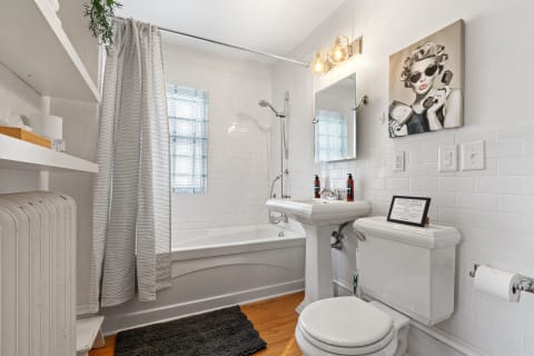 A contemporary bathroom with white subway tiles, a bathtub, pedestal sink, and playful wall art.